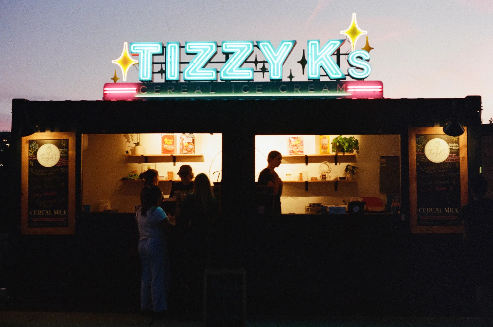 An ice cream shop at dusk with a bright neon light.