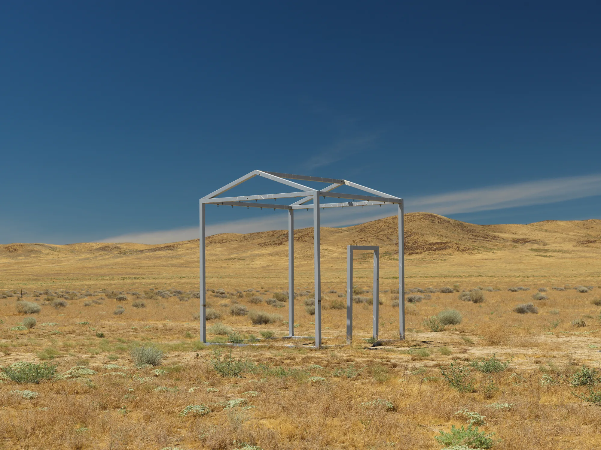 The frame of a house, actually an art installation, is seen on a baren background.